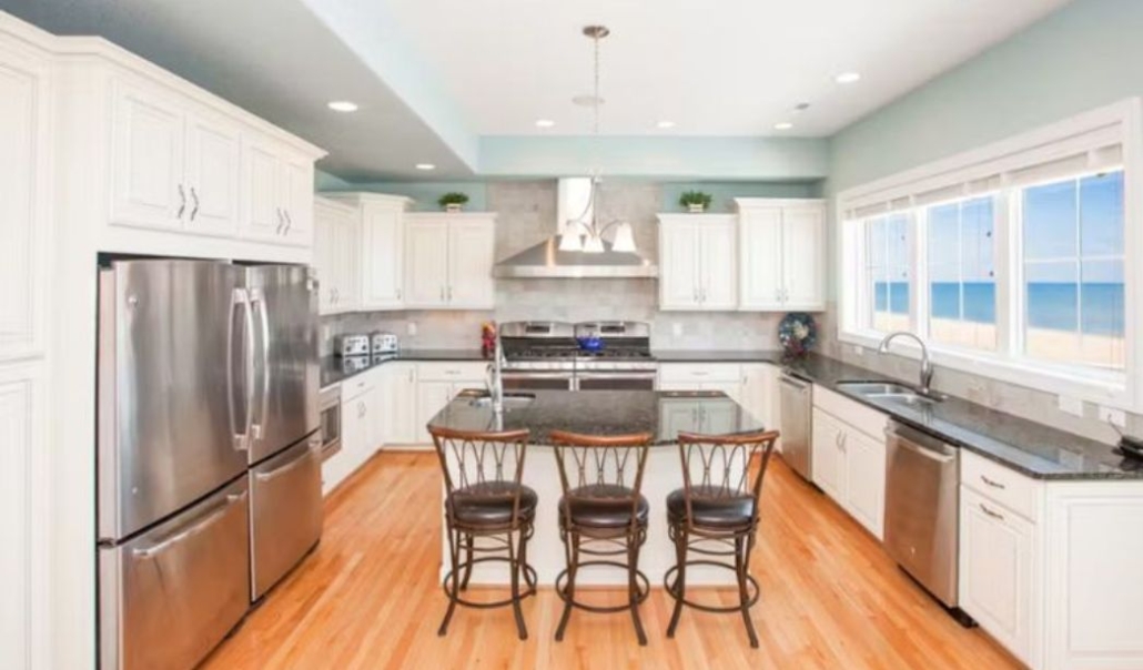 The Over the Moon custom kitchen features white cabinetry, sleek black countertops, large windows with overlooking view of the sea