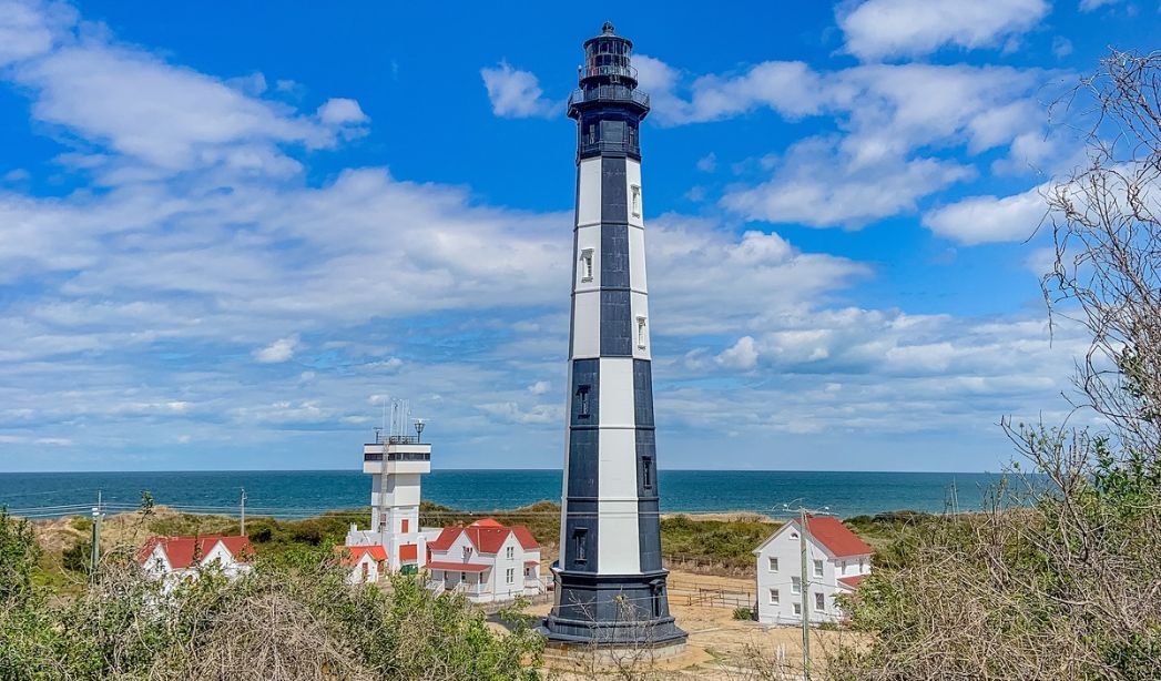  Cape Henry Lighthouse stands atop a hill overlooking the ocean, a historic landmark in Virginia Beach's scenic landscape.