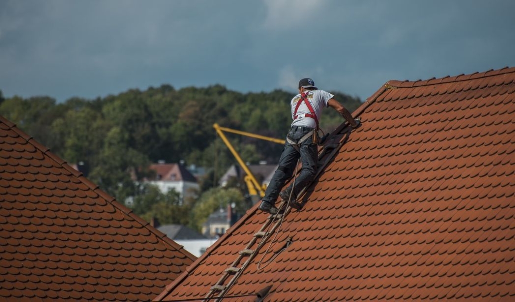 A man on a ladder conducting a roof inspection, highlighting the importance of seasonal home maintenance for property safety.