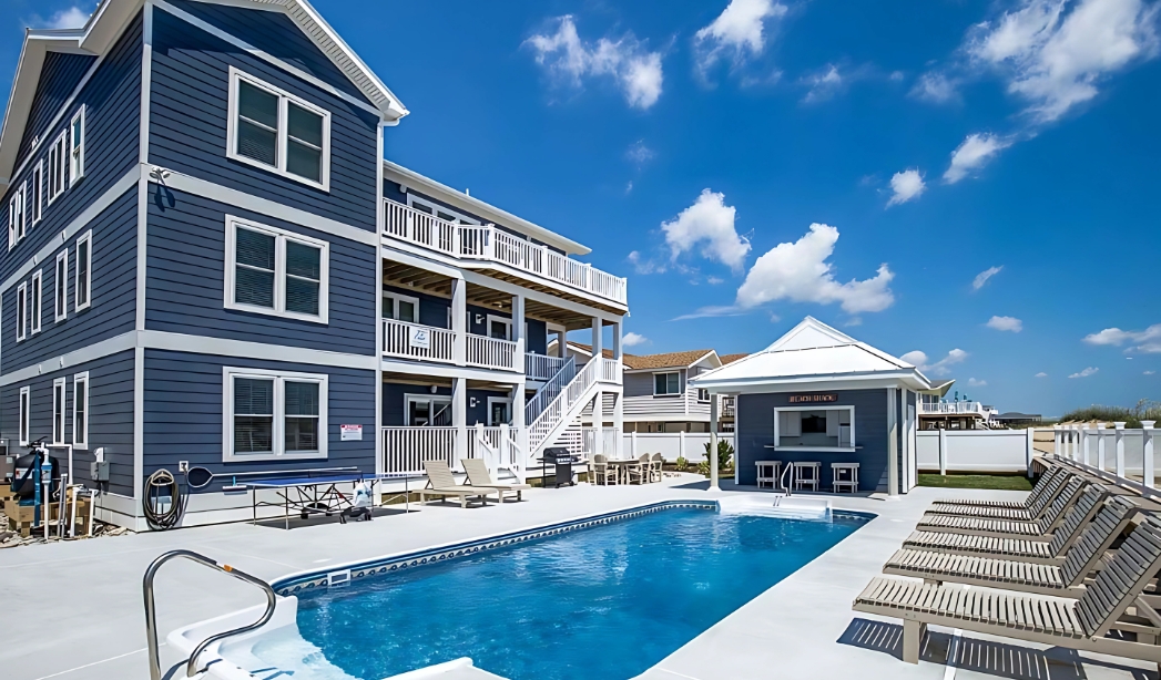 A blue residence with a pool and deck chairs, exemplifying the work of Great Neck Virginia Beach Home Builders.