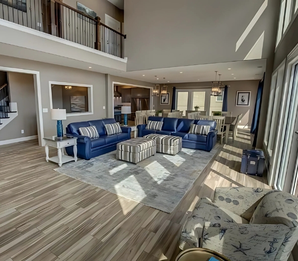 Large living room with blue couches and a staircase, exemplifying the innovative designs of Alanton Virginia Beach Home Builders.