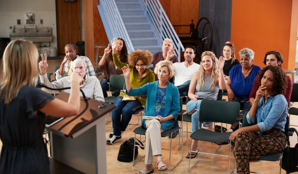 A group of people with hands up in a room, actively joining lifelong learning opportunities in Virginia Beach.