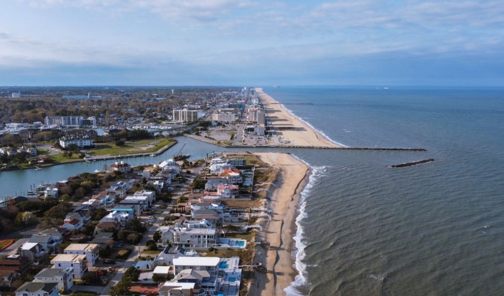Aerial view of Virginia Beach, showcasing the sandy beach and the surrounding town with buildings and greenery.