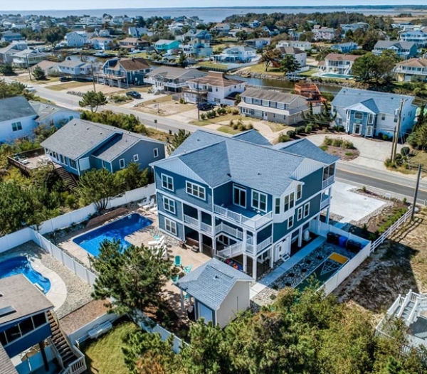 Aerial view of a beach house with a pool, showcasing the coastal landscape and surrounding area.