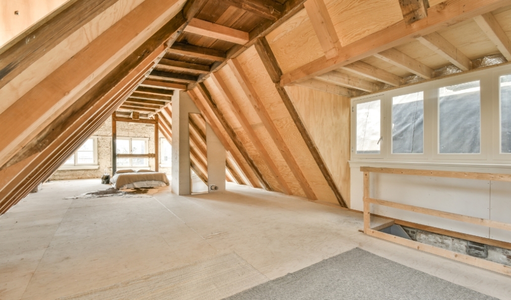 An attic with rustic wood beams and a window, highlighting options for interior conversions in Virginia Beach.