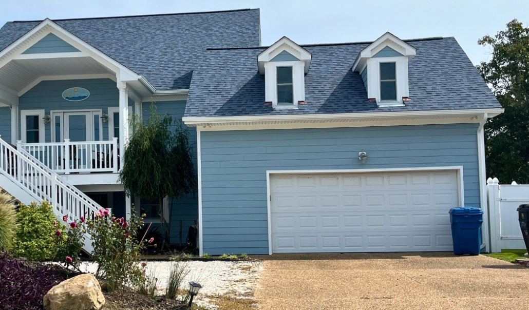 A blue house with a white garage and blue roof, illustrating a home remodel focused on garage door replacement.