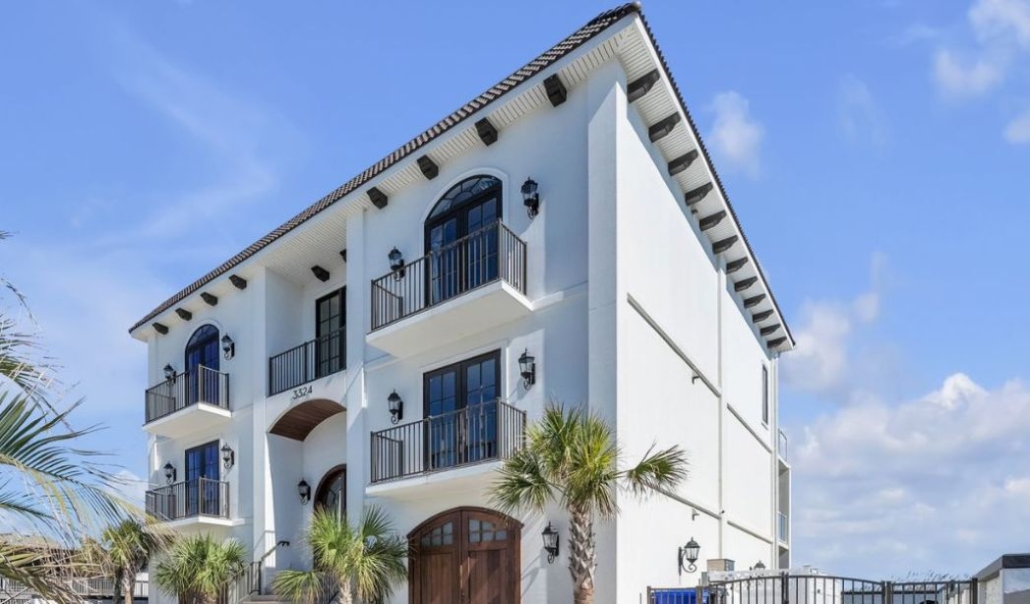 Elegant three-story Mediterranean-style home with white stucco exterior, black rail balconies, and palm trees in front under a clear blue sky.