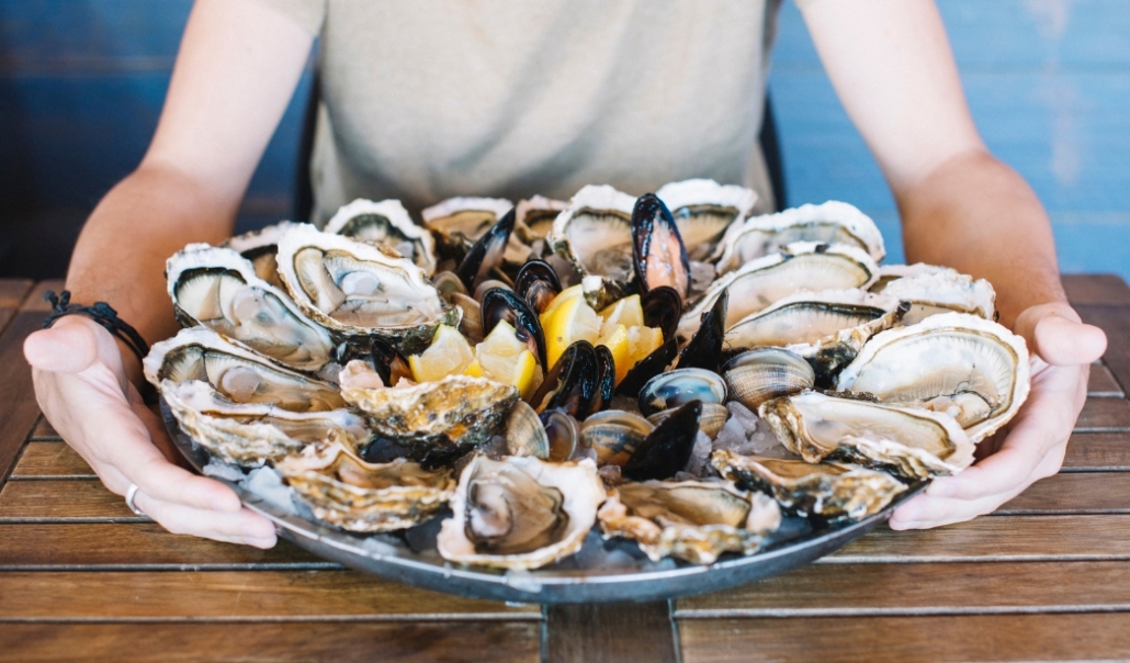 A person holds a plate of fresh oysters, celebrating local oyster season in Virginia Beach during November.