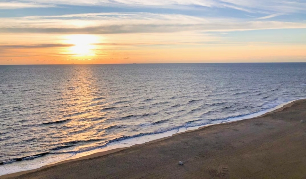 A serene Virginia Beach sunset in November, with the sun dipping below the ocean horizon, casting warm colors across the sky.