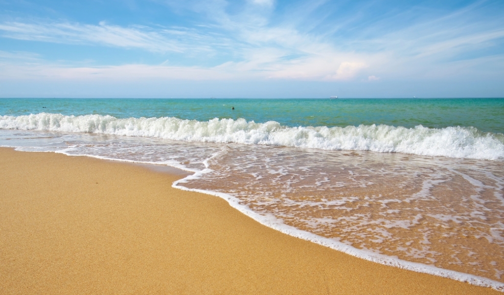 A sandy beach at Sandbridge, Virginia, with gentle waves lapping under a clear blue sky.
