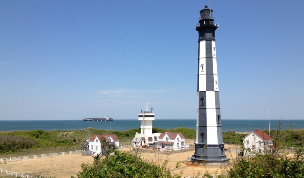 A prominent Cape Henry Lighthouse with a tall tower and a houses, highlighting Virginia Beach's maritime history.