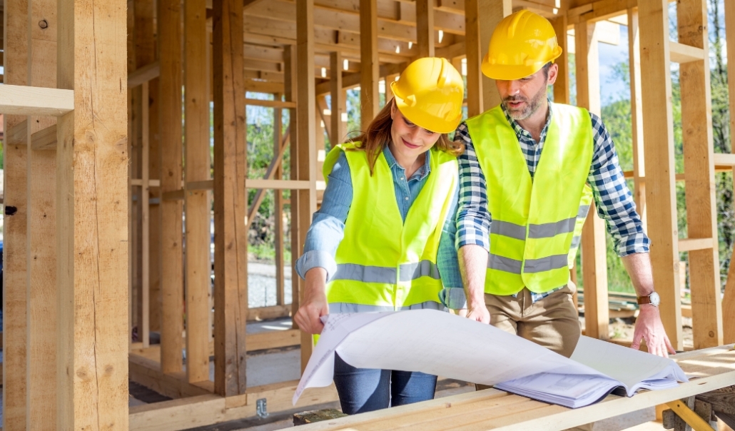 Two construction professionals in hard hats examining architectural plans for a custom home project.