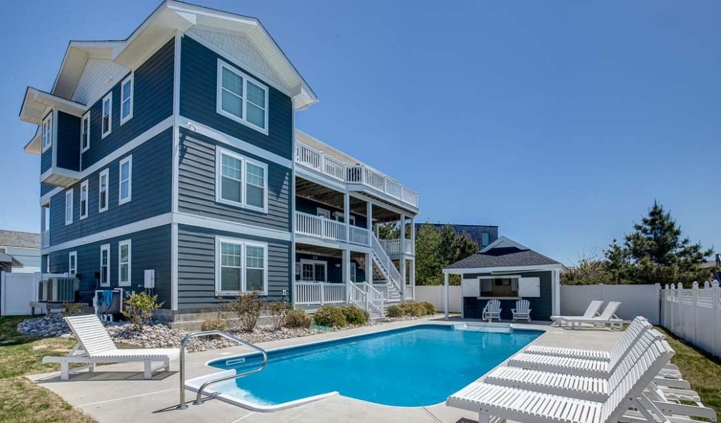 Exterior view of a spacious blue house with a pool, representing Bay Colony Virginia Beach Home Builders' relaxing design.