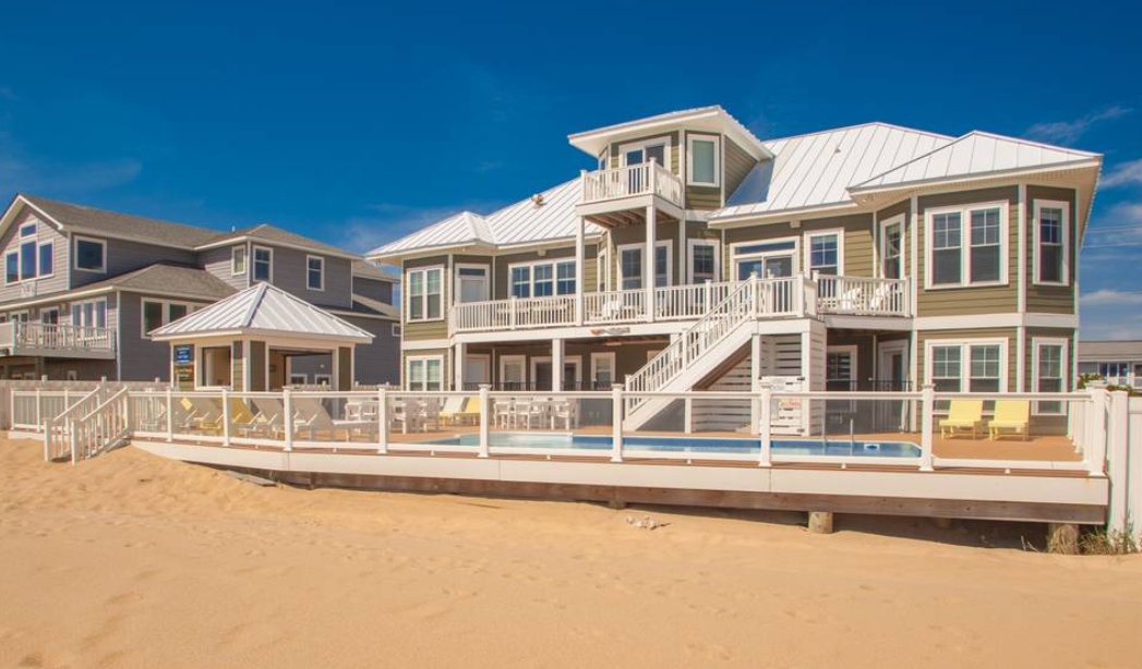 A beach house with a deck and stairs leading to the sandy beach, showcasing coastal living by Castleton Virginia Beach Home Builders.