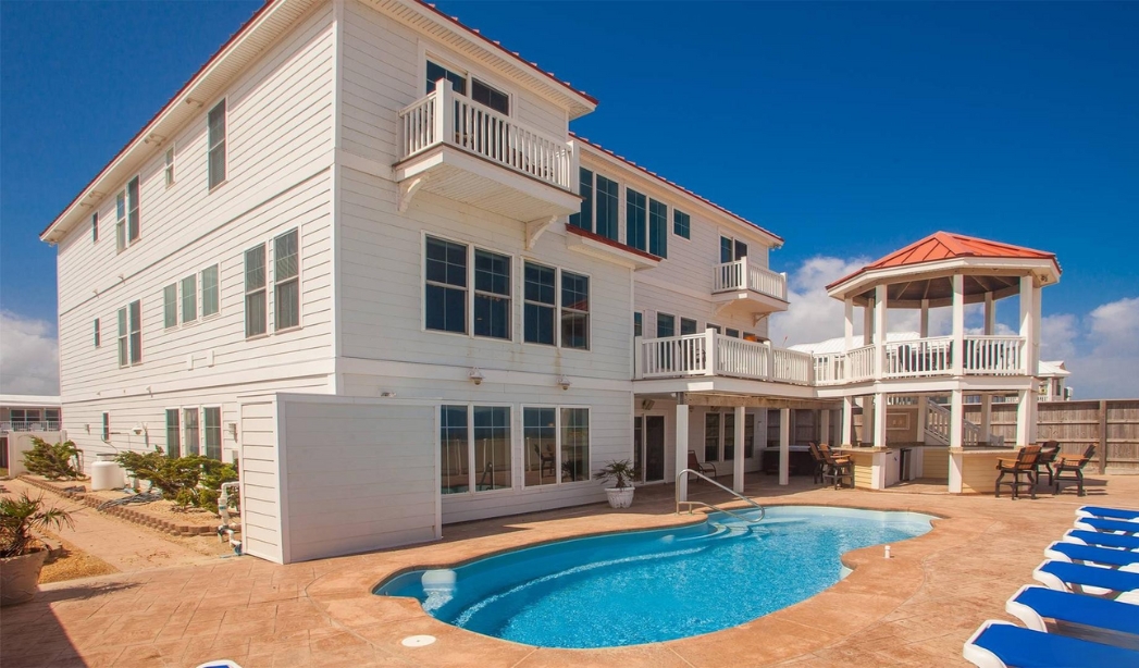 A large white house with a pool and sun deck, showcasing the Oceanic Serenade by Courthouse Estates in Virginia Beach.