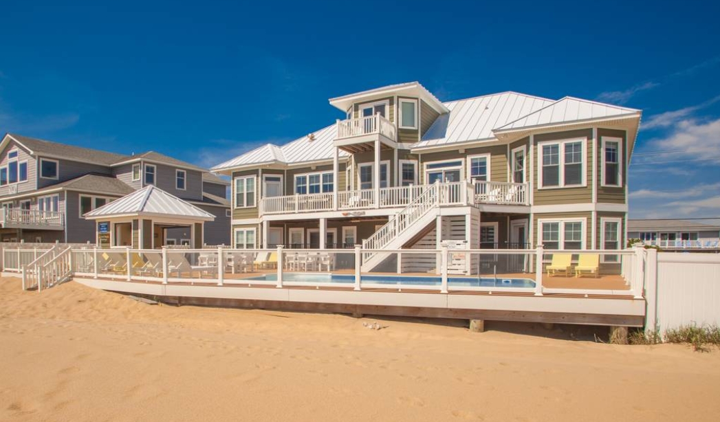 A beach house with a deck and stairs leading directly to the sandy beach, showcasing coastal living in Virginia Beach.
