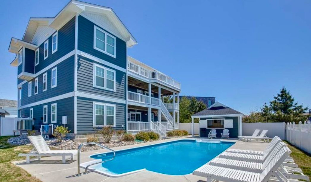 Spacious blue home with a pool and deck, highlighting the "A License to Chill" theme by Nimmo Virginia Beach Homebuilders.