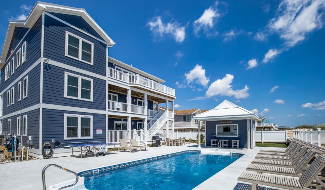 A blue house with a pool and deck, showcasing the Villa Sol by Strawbridge Virginia Beach Homebuilders.
