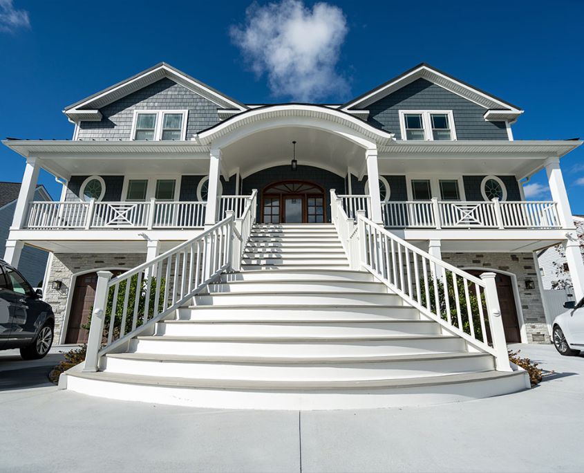 A custom-built coastal residence featuring a dramatic front staircase, expansive covered porch, and durable exterior finishes, reflecting RBC Homes’ craftsmanship in creating elegant.