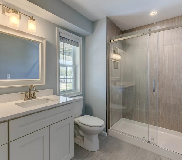A functional bathroom upgrade featuring a sleek glass-enclosed shower, spacious white vanity, large mirror, and soft lighting, showcasing RBC Homes’ focus on modern design, efficiency, and everyday comfort.