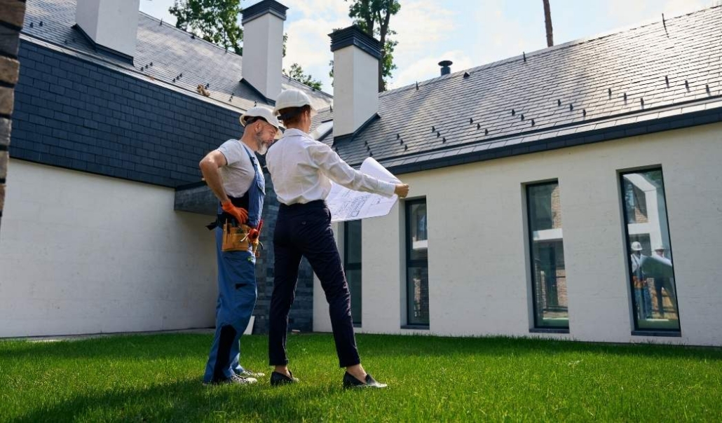 Two individuals stand with blueprints, planning a garage conversion to a home office outside a house.