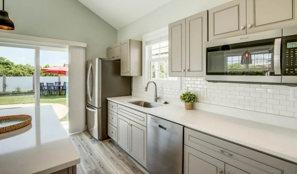 A modern kitchen featuring stainless steel appliances and white cabinets, part of a garage conversion to a home office.