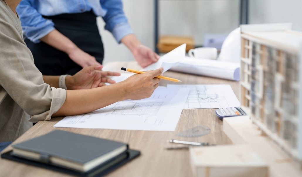 Two individuals reviewing architectural plans at a desk, focusing on the timeline for converting a garage to a home office.