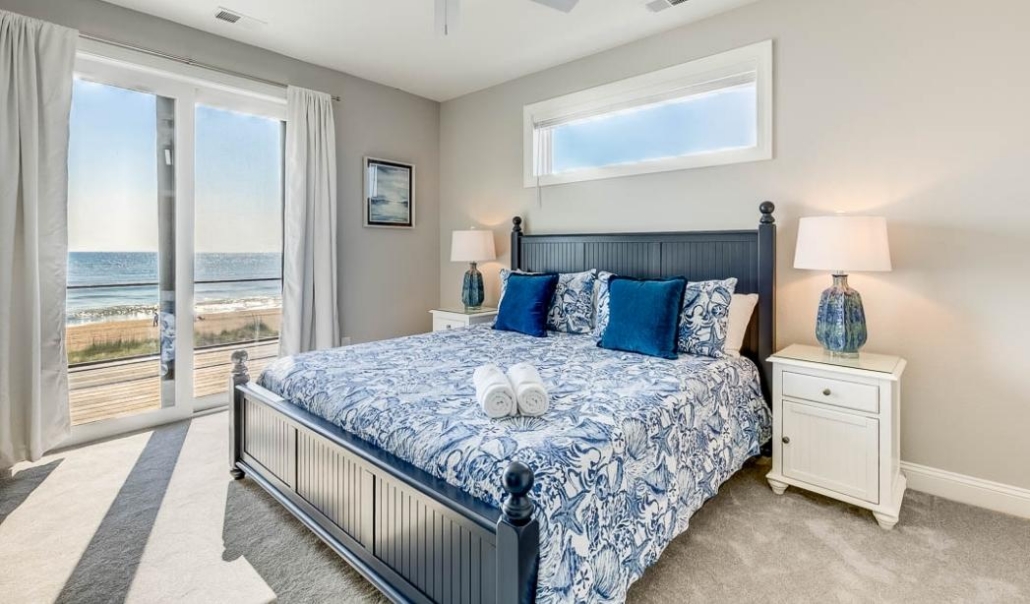 Elegant master bedroom with a blue and white bed, offering a beautiful ocean view, designed for coastal living.