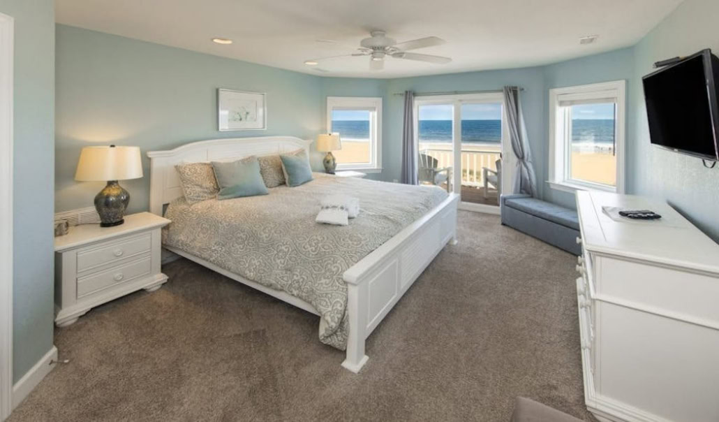 Spacious bedroom with a king-size bed, ocean views, and balcony access in a coastal home.