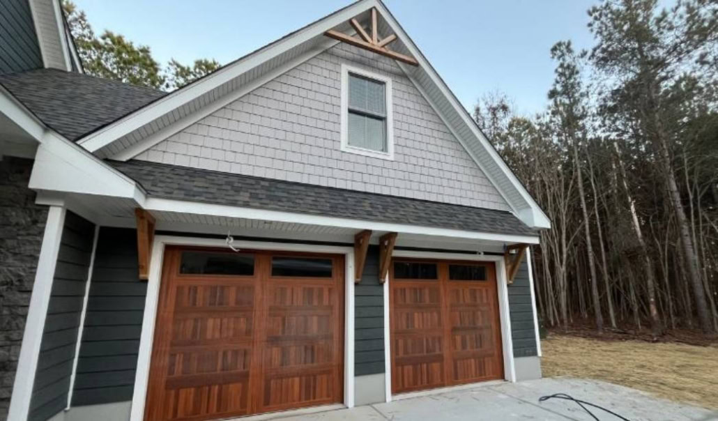 Detached garage addition with two wooden doors, gray siding, and a shingled gable roof.
