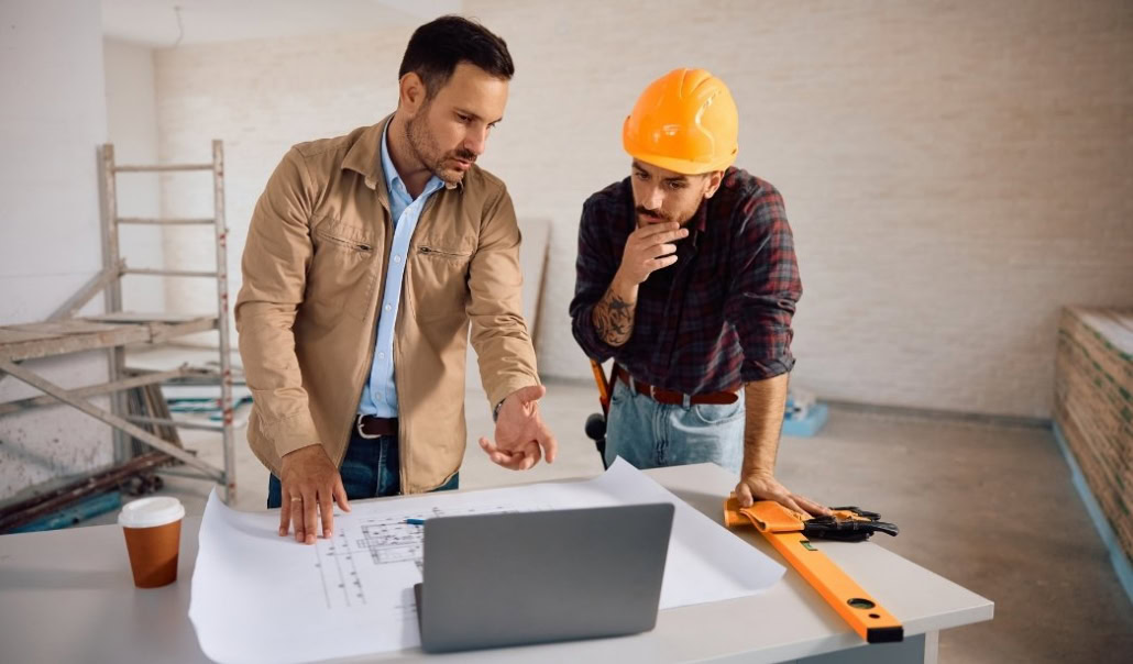 Contractor and construction worker reviewing plans to decide whether to renovate or rebuild a home.